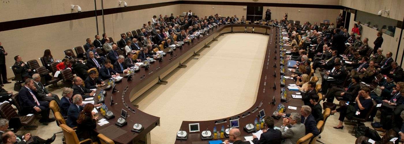 NATO officials and military representatives are meeting around a large conference table, discussing alliance strategy and collective security