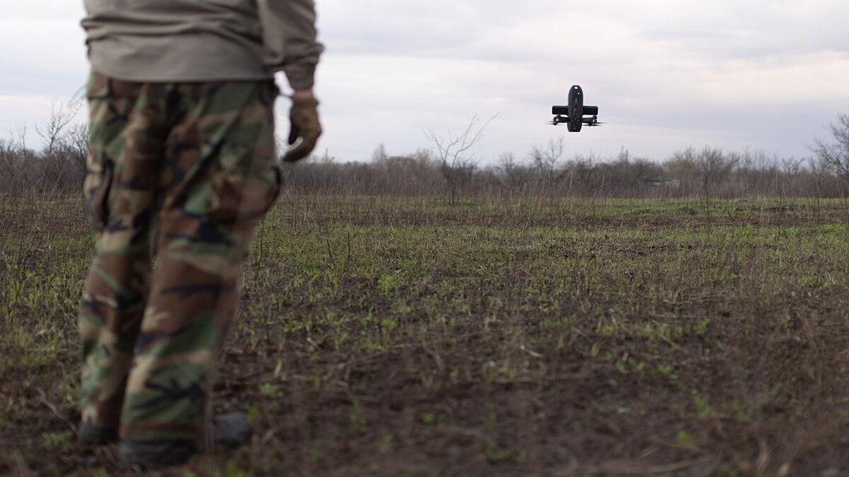 A small drone flying over an open field during a military field operation